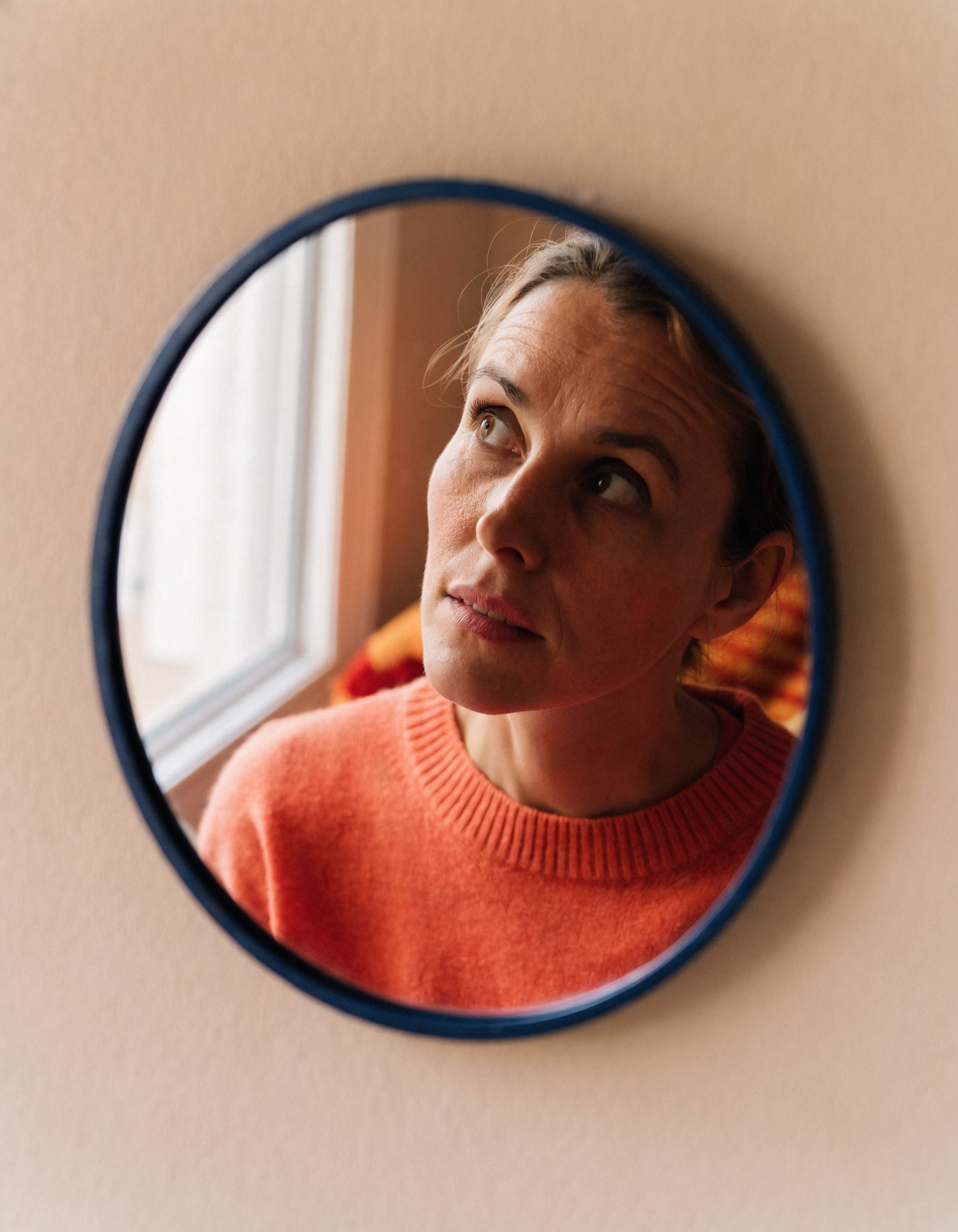 O oglindă rotundă, ușor aburită la margini, în care se vede un chip calm — nu perfect, ci prezent; lumina vine din inter